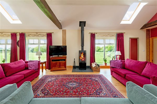 3 sofas around the wood burning stove and windows overlooking fields